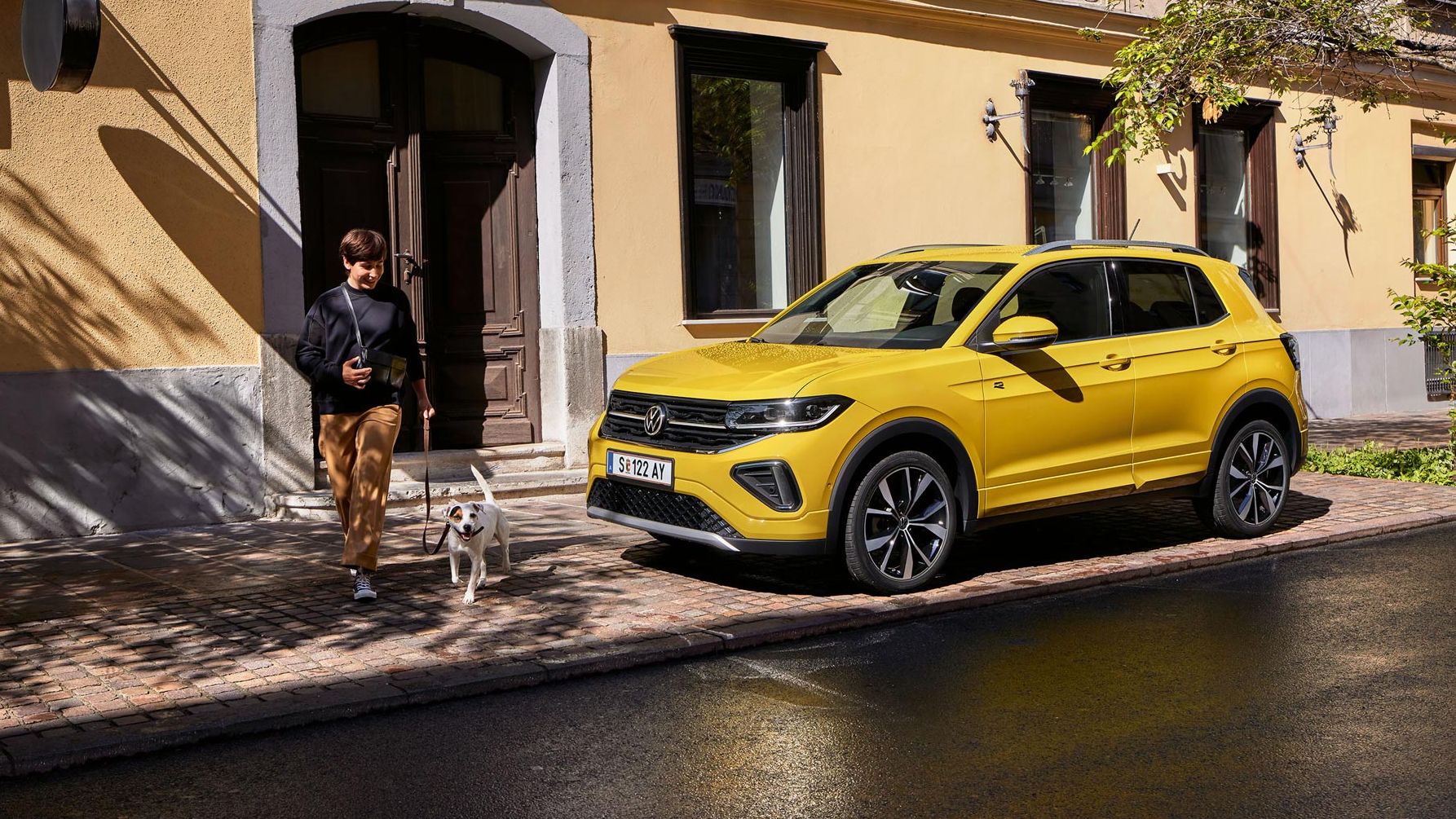 VW T-Cross parkt am Straßenrand, Frau mit kleinem Hund geht an ihm vorbei