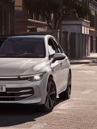 Weißer VW Golf fährt auf einer Straße auf eine Kreuzung zu.