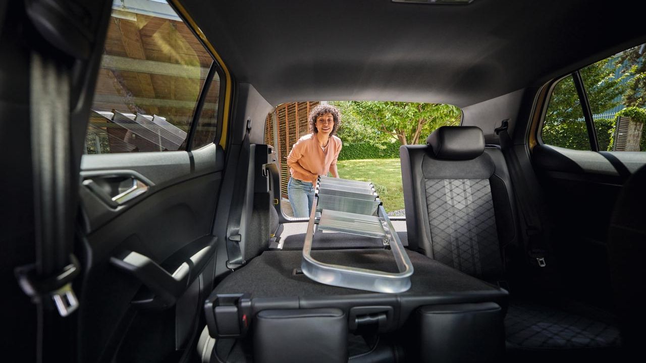 Eine junge Frau schiebt eine Leiter über den umgeklappten Rücksitz in einen VW T-Cross.