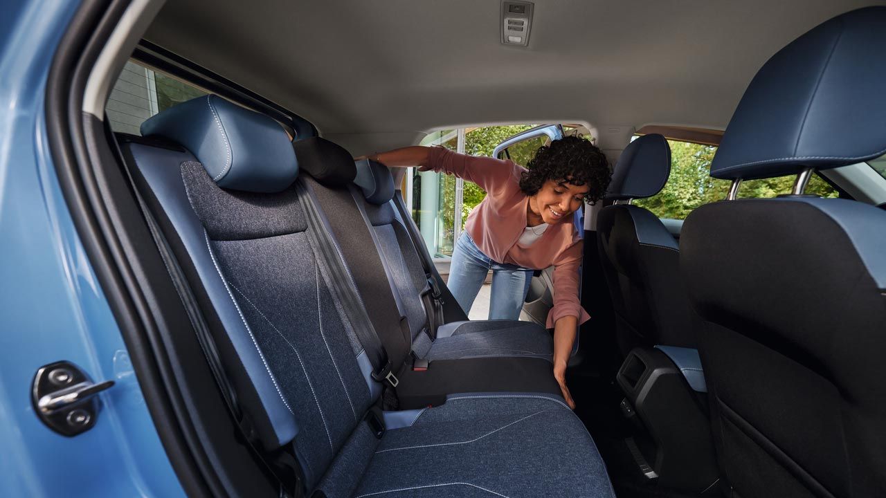 Eine junge Frau klappt die Lehne des Rücksitzes eines VW T-Cross um.