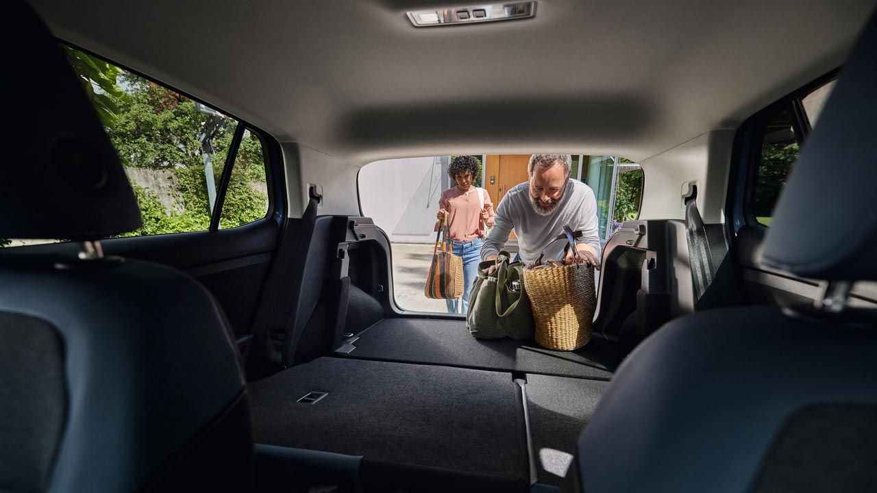 Blick von den Vordersitzen auf die umgeklappten Rücksitze und Kofferaum eines VW T-Cross. Ein Mann lädt Taschen ein.