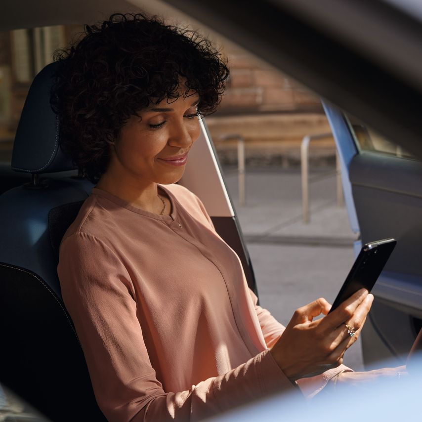 Eine lächelnde Frau sitzt auf dem Fahrersitz eines VW T-Cross und schaut auf ihr Smartphone.