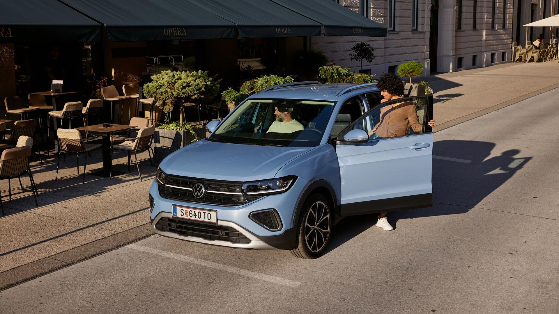 Eine Frau steigt in einen blauen VW T-Cross, der vor einem Straßencafé parkt.